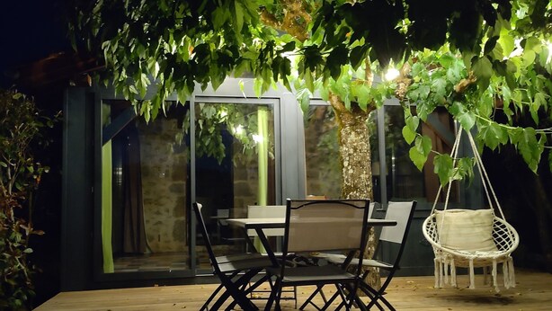 An outdoor patio with a table and chairs, surrounded by greenery and a hanging chair. - Maison en pierre avec piscine – Nature & calme en Vallée de la Dordogne (Bilhac)