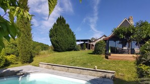 A backyard with a swimming pool, a wooden deck, and a house with a covered patio. - Maison en pierre avec piscine – Nature & calme en Vallée de la Dordogne (Bilhac)