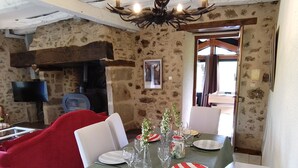 A dining area with a stone wall, a chandelier, and a television. - Maison en pierre avec piscine – Nature & calme en Vallée de la Dordogne (Bilhac)