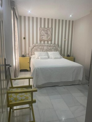 A bedroom with a striped wall, a bed with white bedding, a headboard with a globe design, and a small bedside table. - Entire 2 Bedroom Apartment (Mar del Plata)