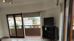 Een ruime woonkamer met een grote schuifpui naar een balkon, een flatscreentelevisie op een standaard en een vloerkleed met een patroon.