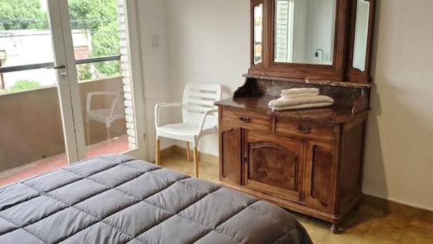Een slaapkamer met een bed, een dressoir met spiegel en een stoel.
