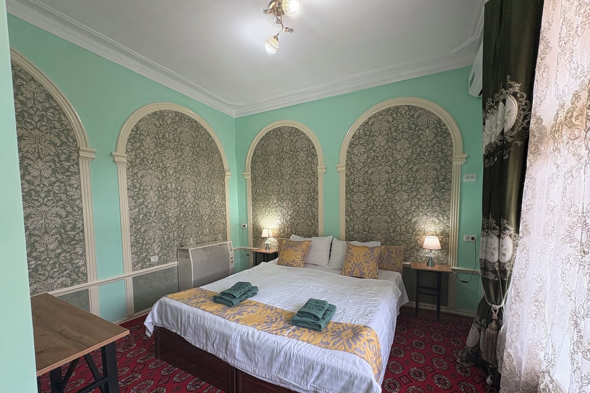 Una camera d'albergo con un letto grande, due comodini, una scrivania e un tappeto decorato.