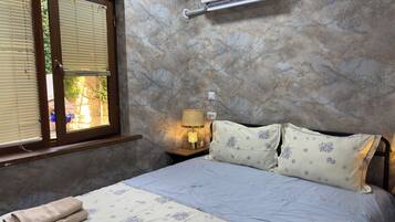 Una camera da letto con un letto, una finestra con persiane, un condizionatore d'aria, una lampada da comodino e una presa a muro.