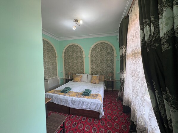 Ein Schlafzimmer mit einem Bett, zwei Nachttischen, einer Deckenleuchte und gemusterten Vorhängen.