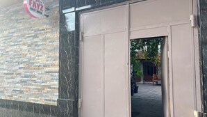 Entrada de un edificio con un letrero que dice 'FAYZ GUEST HOUSE', fachada de piedra y una puerta metálica grande.
