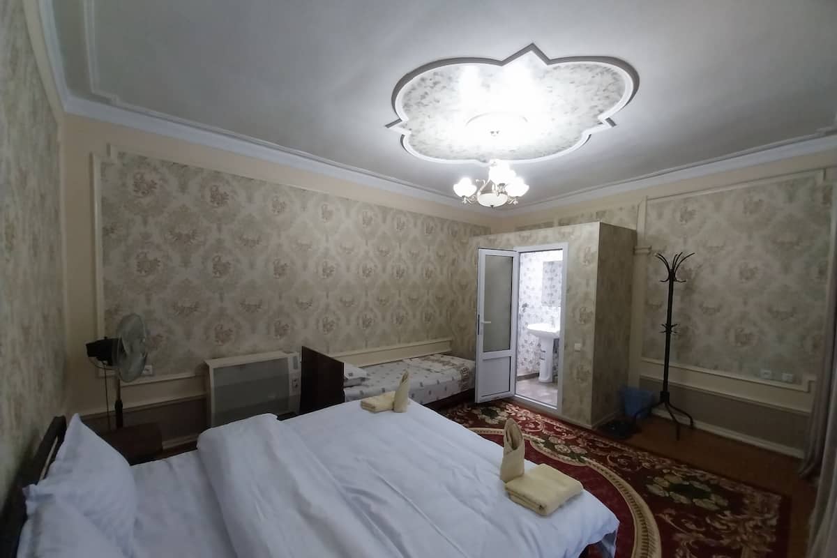 Camera d'albergo con un letto, un termosifone, una ventola a piantana, un armadio, un bagno con un lavandino e un appendiabiti.