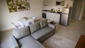 Een moderne woonkamer met een grijze bank, een kleine eettafel en een keuken met een magnetron en fornuis.