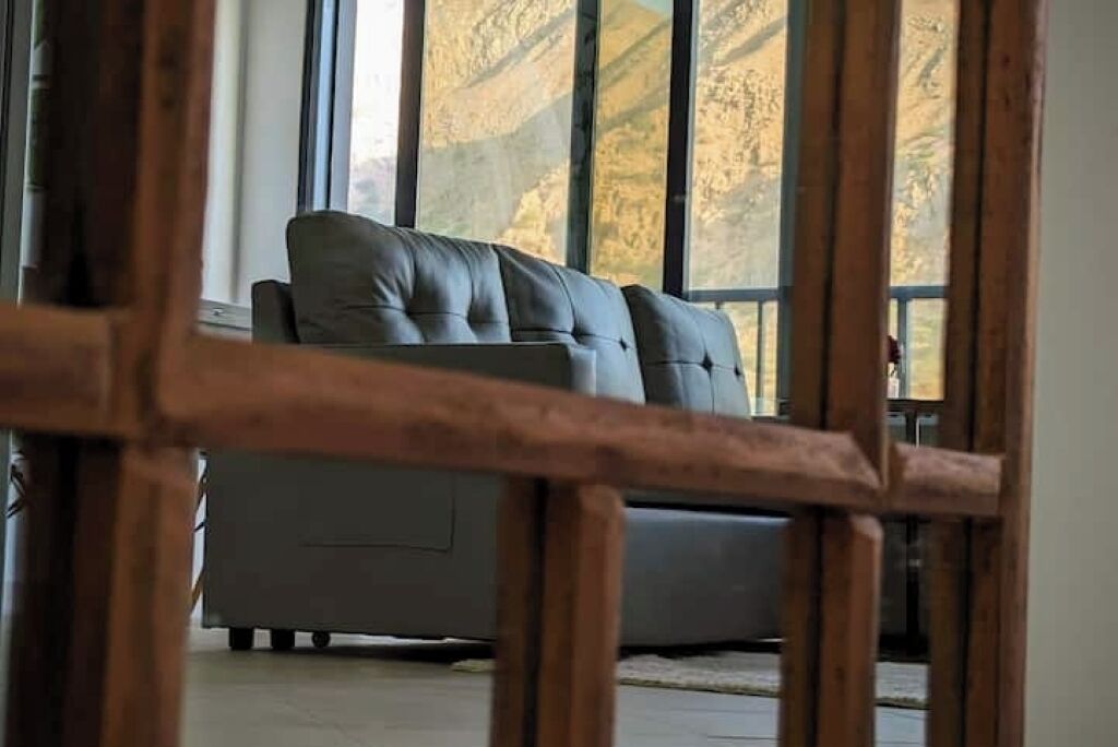 Une pièce avec un canapé gris, de grandes fenêtres et un plancher en bois.