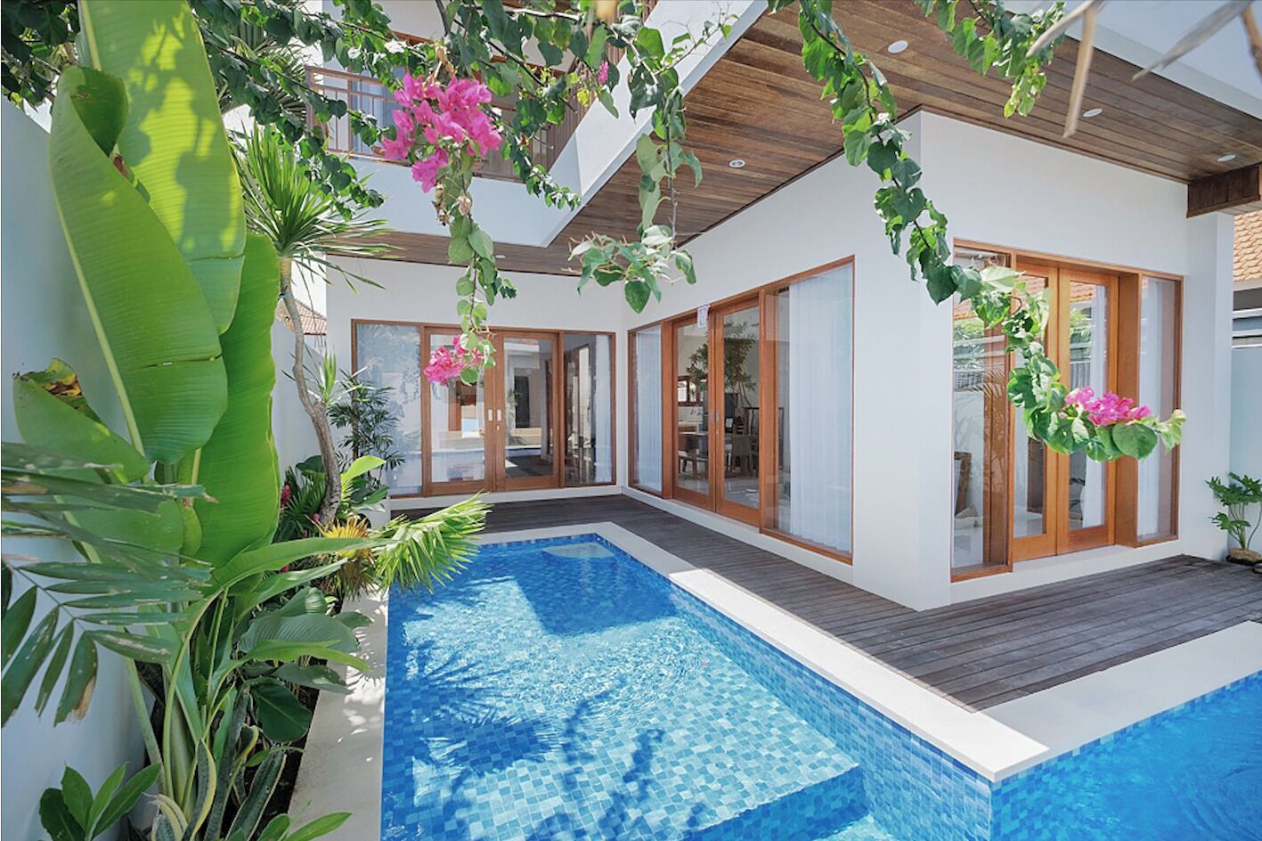 Ein modernes Haus mit Swimmingpool, großen Fenstern und tropischen Pflanzen.