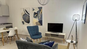 Una sala de estar moderna con un sofá, un sillón azul, un televisor, un comedor y arte abstracto en la pared.