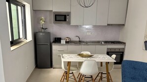 Cocina compacta con refrigerador, microondas, estufa y comedor con sillas y mesa.