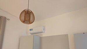 A room with a flat-screen TV, a ceiling-mounted air conditioner, and a woven pendant light. - Tarrafal Bay · 1Bdr Apt · Sea view - 4 (Tarrafal)
