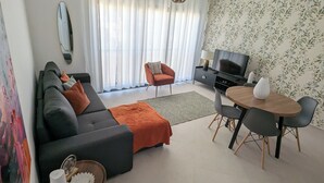 A modern living room with a sofa, armchair, TV, and dining table. - Tarrafal Bay · 1Bdr Apt · Sea view - 4 (Tarrafal)