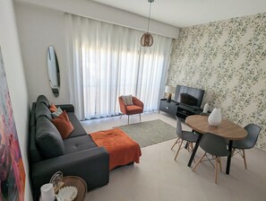 A modern living room with a sofa, armchair, TV, and dining table. - Tarrafal Bay · 1Bdr Apt · Sea view - 4 (Tarrafal)