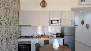 A modern kitchen with a gas stove, oven, microwave, and a dining area with a table and chairs. - Tarrafal Bay · 1Bdr Apt · Sea view - 4 (Tarrafal)