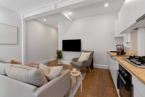 A modern living room with a sofa, a small table, a chair, and a kitchen area with a stove and cabinets. - Chic Bondi Retreat – 10 Min Walk to Beach, modern coastal style (Bondi Beach)