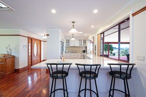 A kitchen with a large island, bar stools, wooden flooring, and a view through the window.