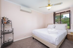 A bedroom with a bed, a ceiling fan, an air conditioner, a window with a view, and a metal shelf unit.