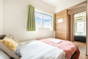 A bedroom with a bed, a window with curtains, a wardrobe, and a door leading to another room. - Haneda 5-chome (Tokyo)