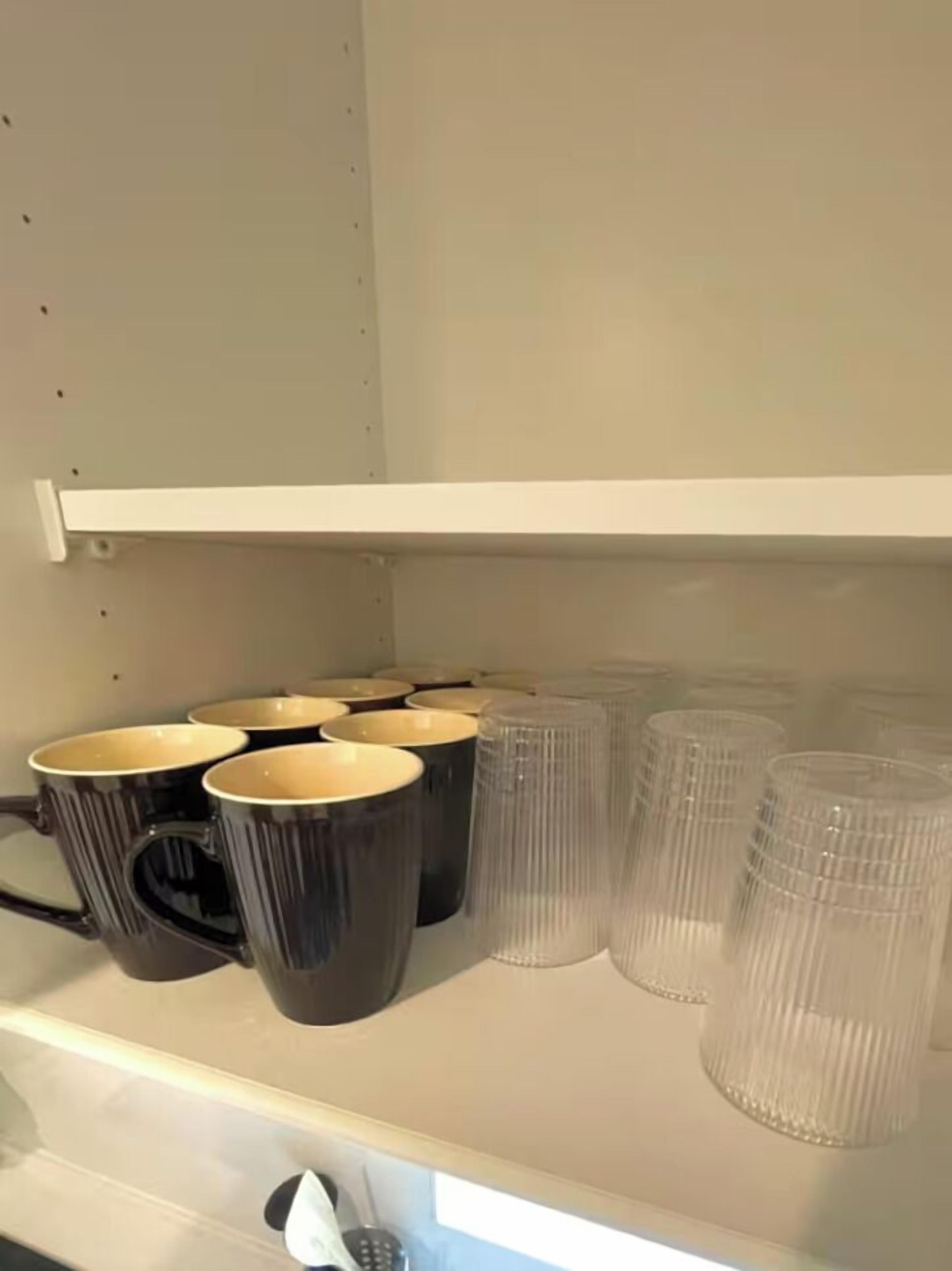 A shelf with black and clear mugs, a white shelf, and a white wall.
