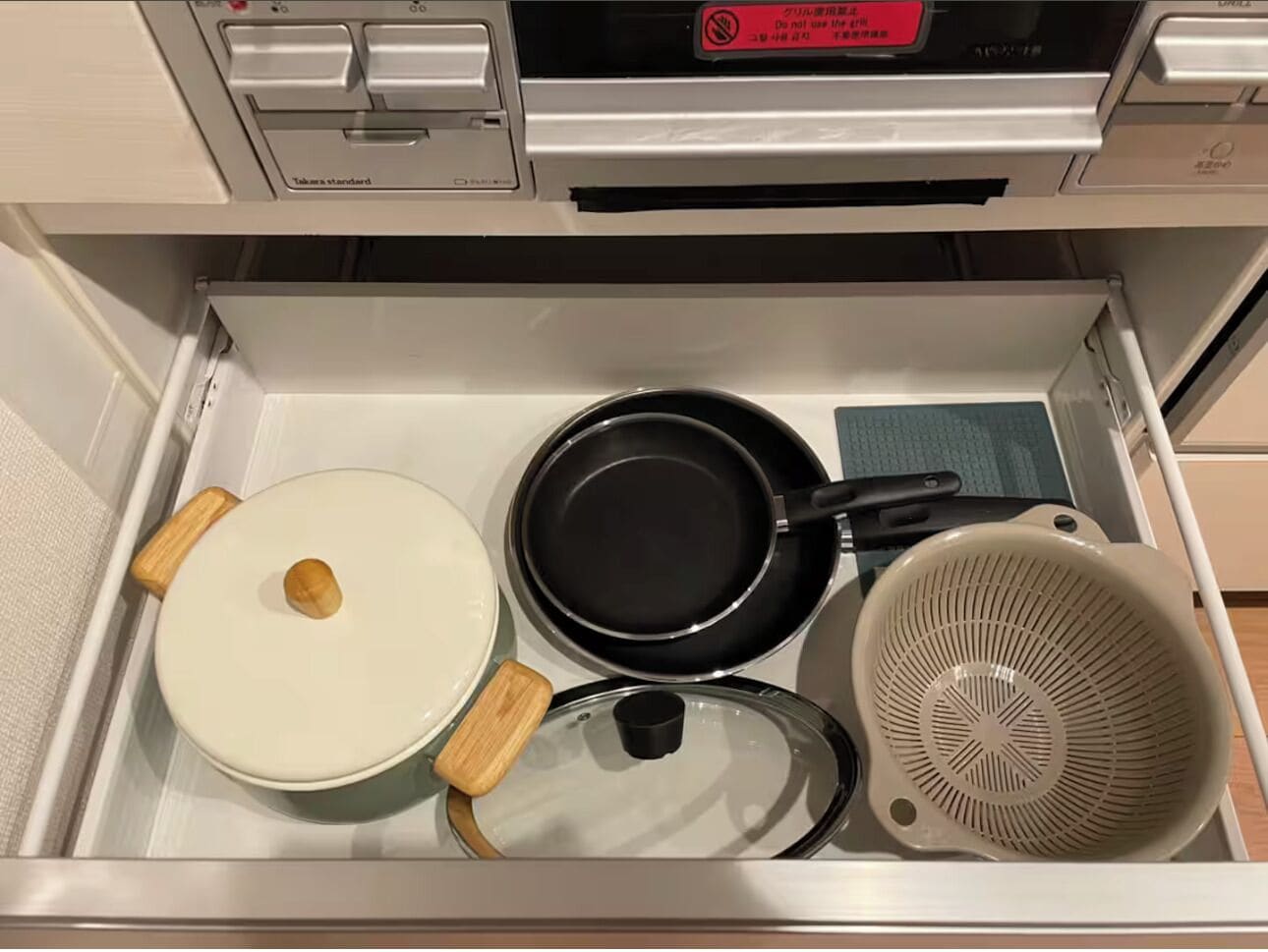 A kitchen drawer with a white pot, a black frying pan, and a colander.