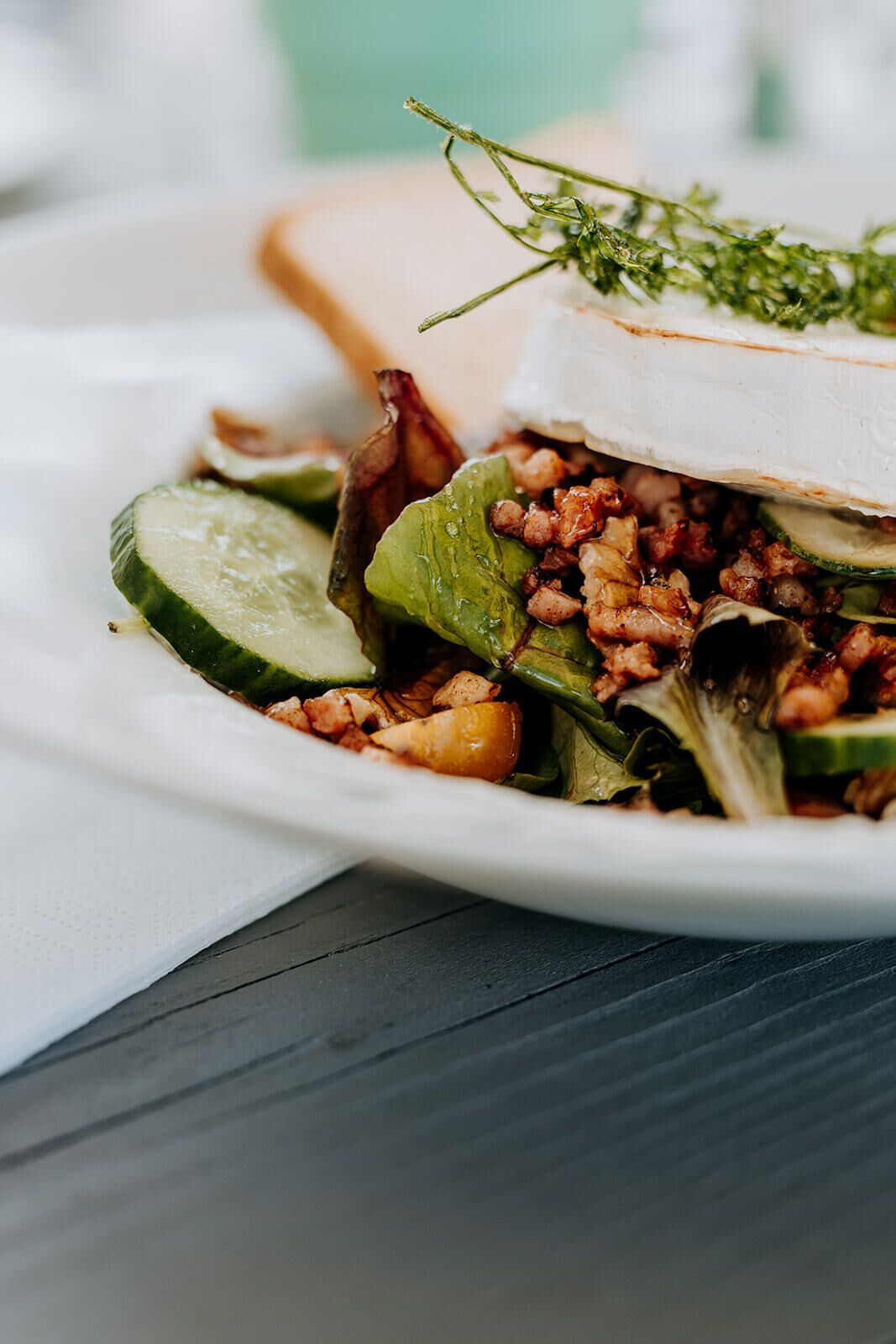 A plate with a sandwich, sliced cucumbers, and a sprig of herb.