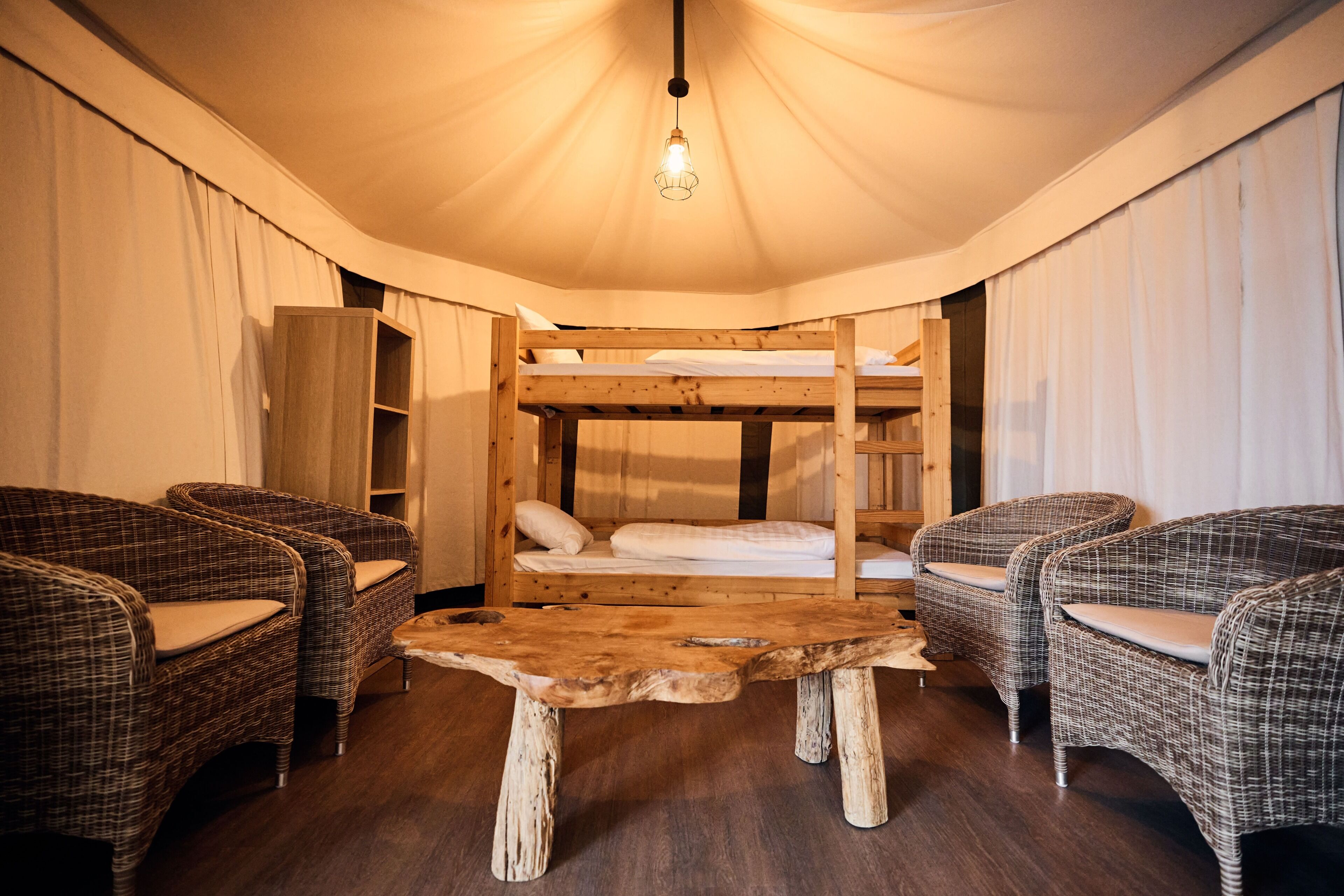 A room with a bunk bed, wicker furniture, a wooden table, and a hanging light fixture.
