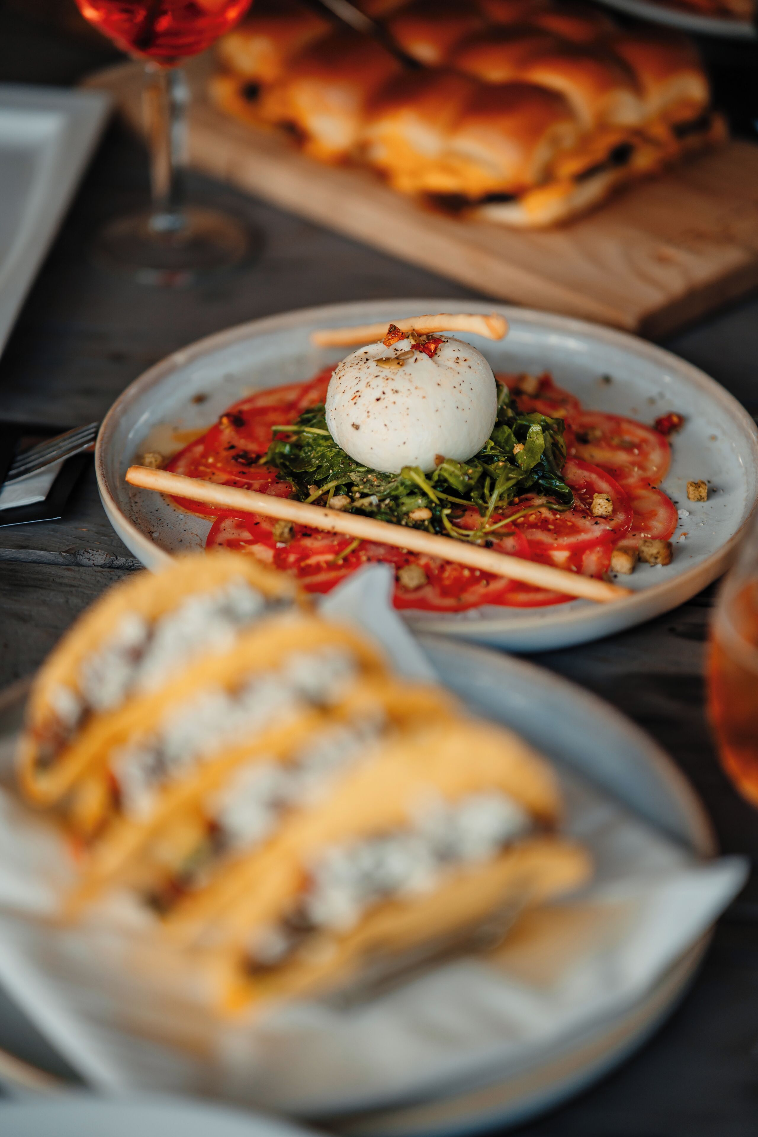 A dining table with a plate of food, a glass of red wine, and a basket of bread.