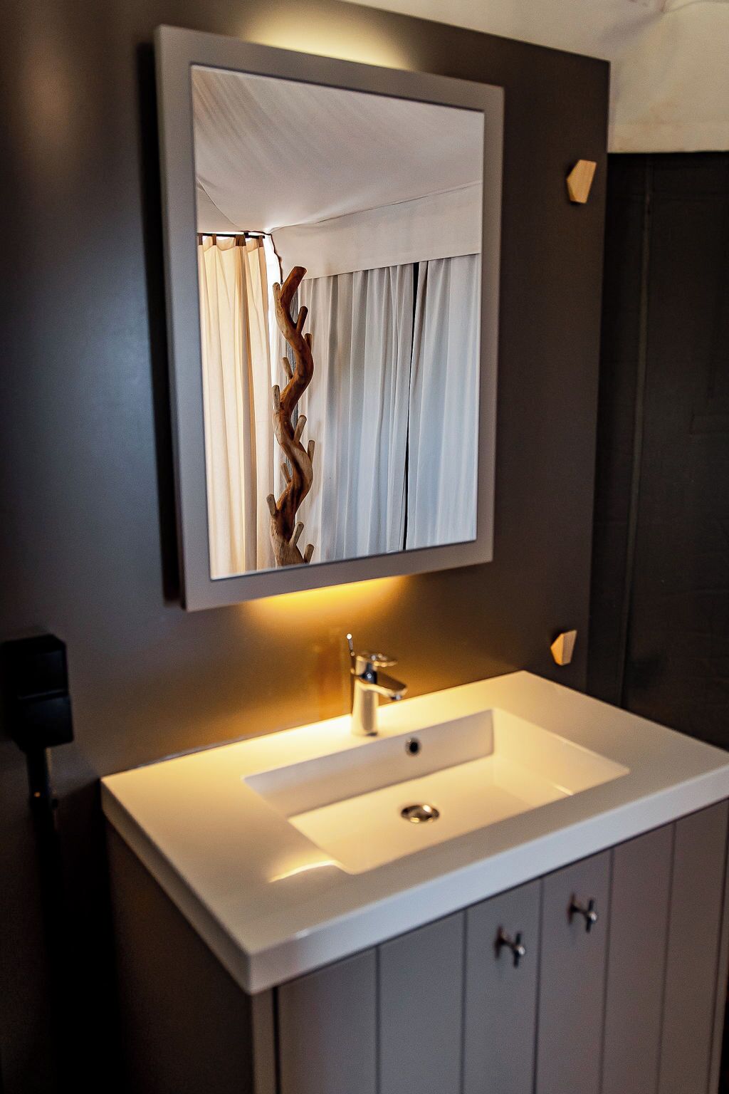 A modern bathroom with a white sink, a mirror above it, and a dark wall.