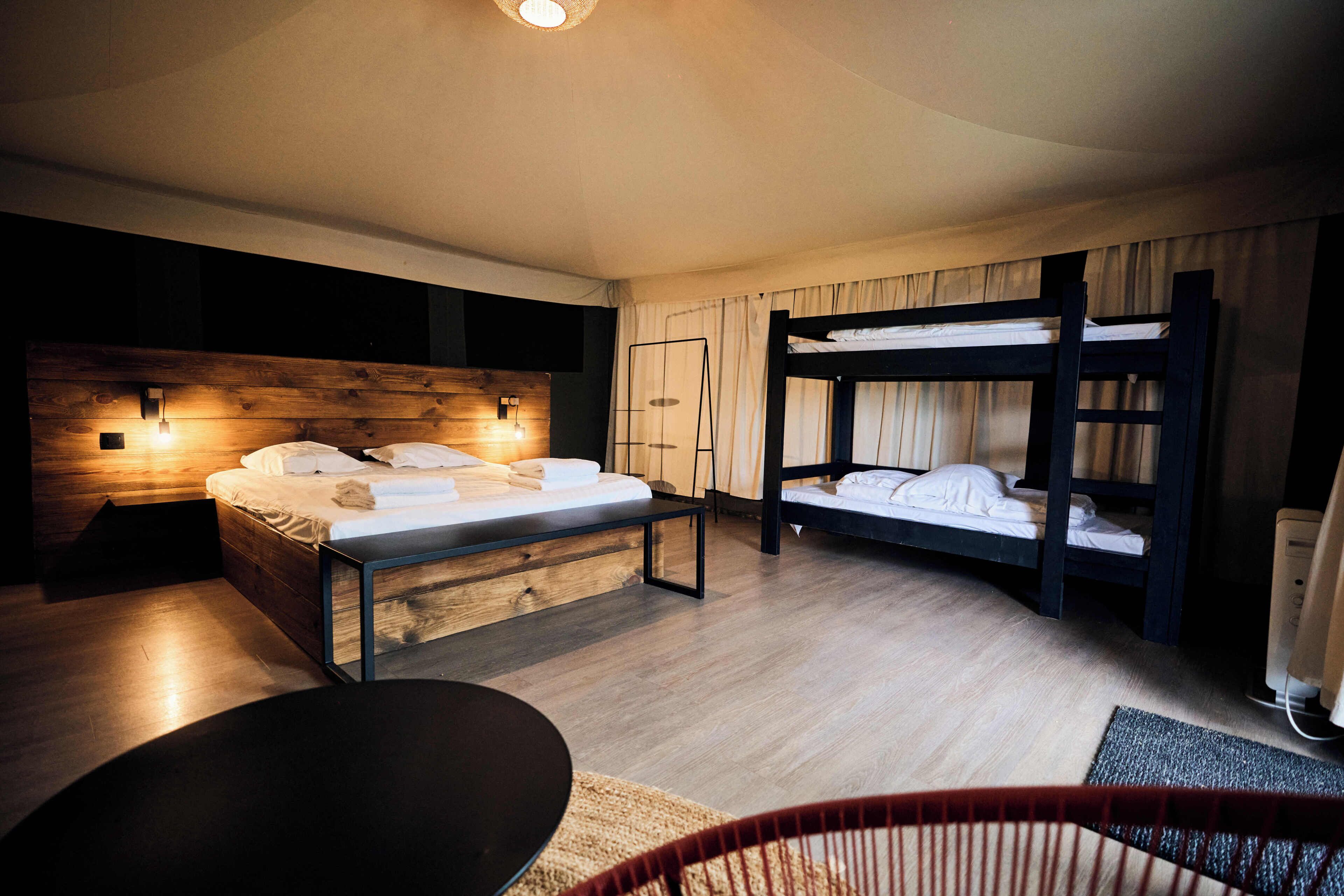 A modern hotel room with a wooden headboard, a bunk bed, a desk, and a chair.