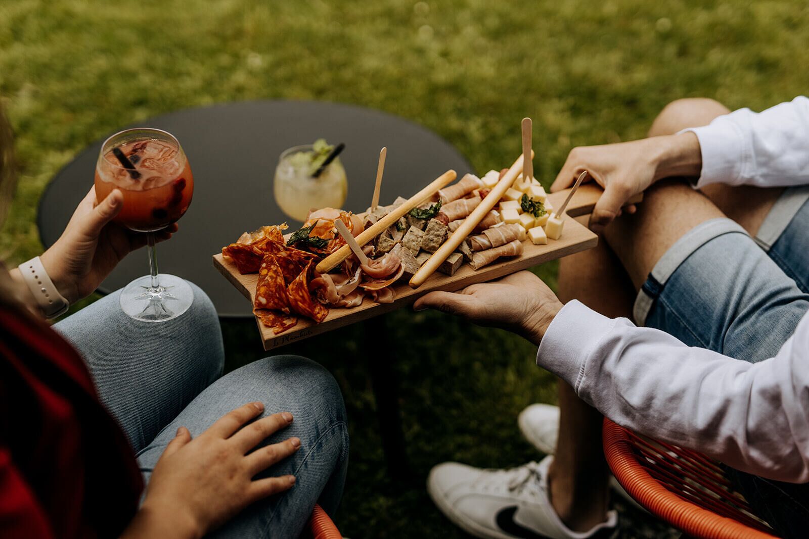 Iemand houdt een schaal vast met verschillende soorten eten en een drankje, zittend buiten.