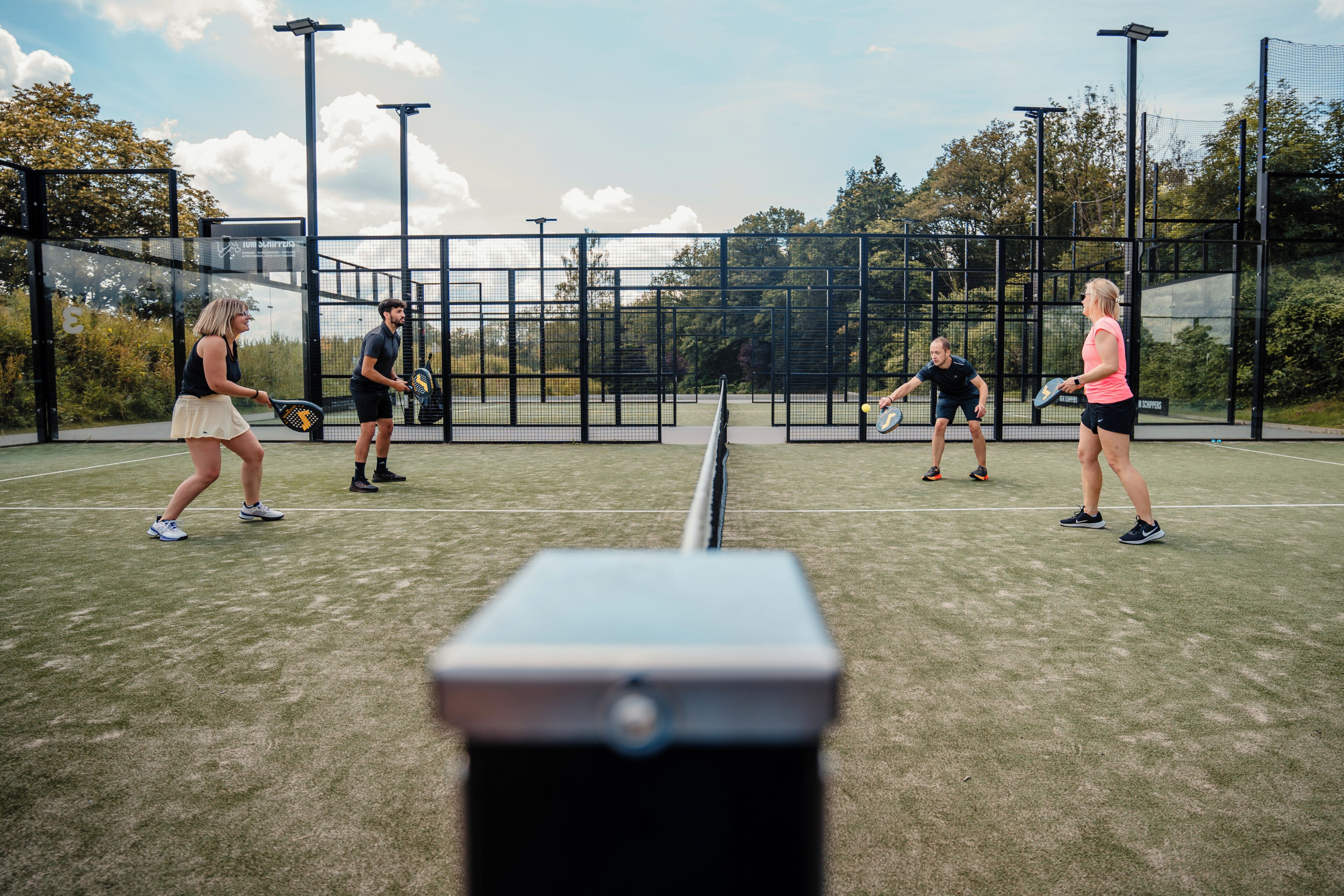 Tenniskenttä, jossa on neljä pelaajaa, verkko ja aita.