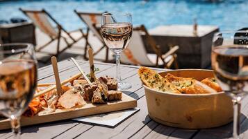Une table en bois installée au bord de la piscine, avec un panier de pain et des verres de vin.
