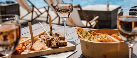 A poolside dining setup with a wooden table, a bowl of bread, and glasses of wine.