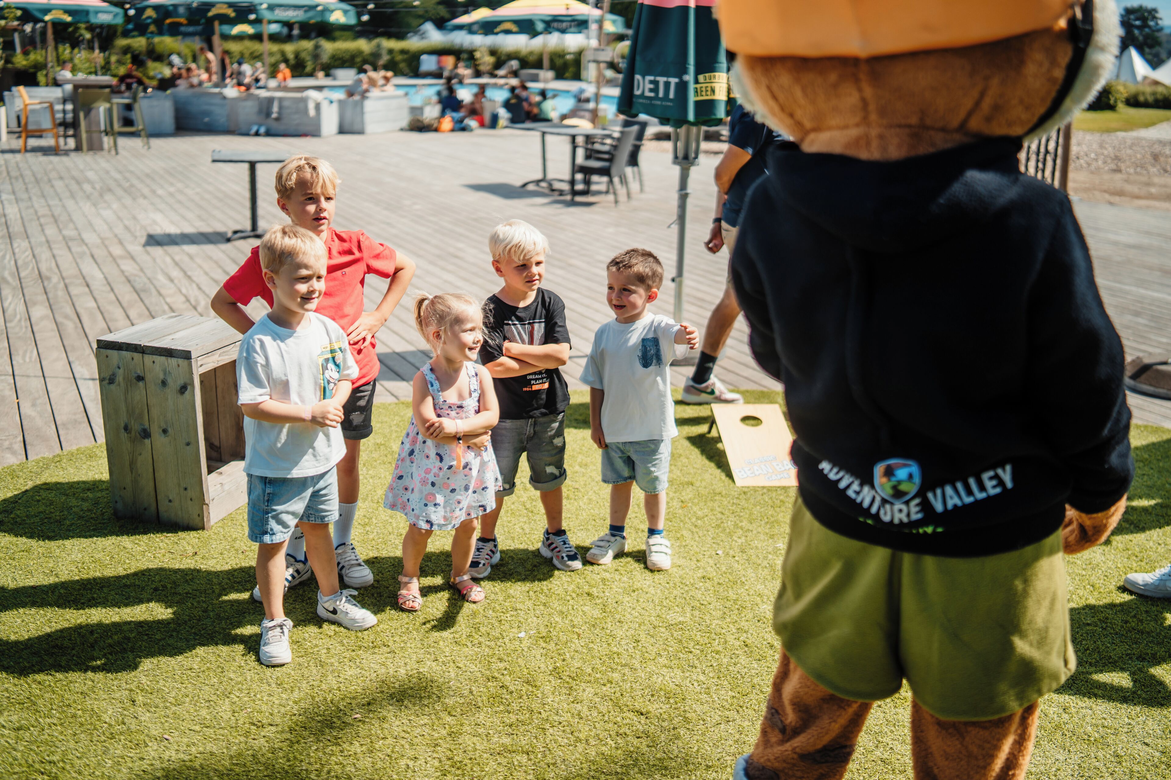A group of children standing on a wooden deck with a mascot in the foreground.