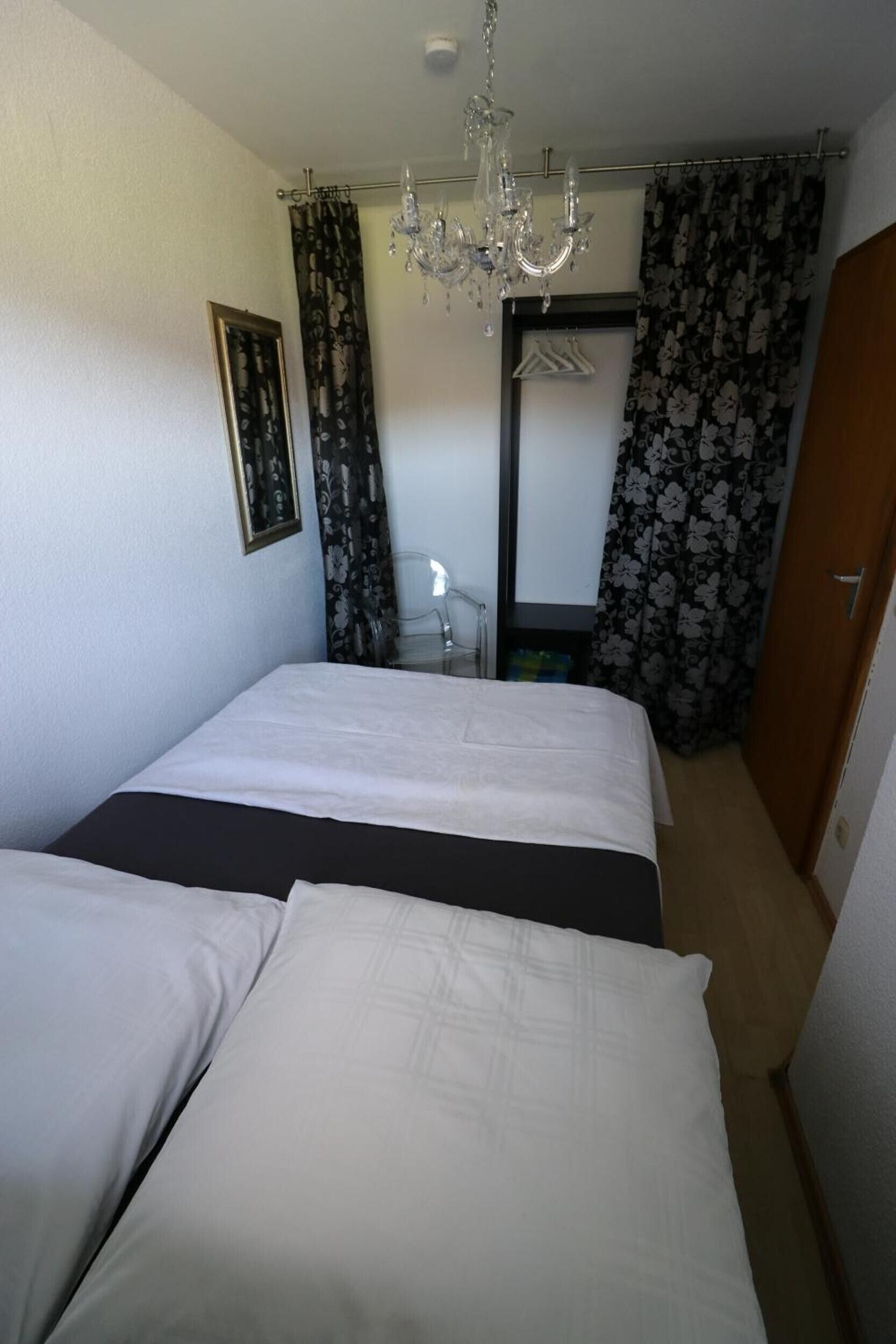 A bedroom with two beds, a chandelier, a mirror, and a wardrobe.