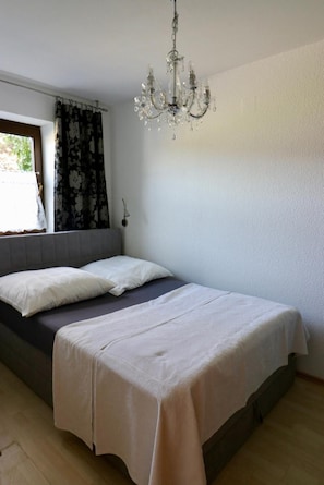 Un dormitorio con cama, candelabro, ventana con cortinas y vistas a la vegetación.