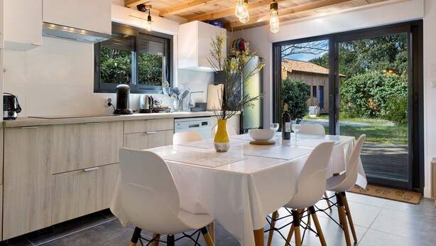 A modern kitchen with a dining area, wooden ceiling, and large windows. - Chalet "Seafront" with Private Terrace, Garden and Wi-Fi (Le Verdon-sur-Mer)