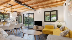 A modern interior with a dining area, yellow sofa, TV, and a kitchen. - Chalet "Seafront" with Private Terrace, Garden and Wi-Fi (Le Verdon-sur-Mer)