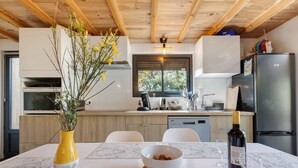 A modern kitchen with a dining table, a vase with flowers, a bowl of nuts, a wine bottle, and glasses. - Chalet "Seafront" with Private Terrace, Garden and Wi-Fi (Le Verdon-sur-Mer)
