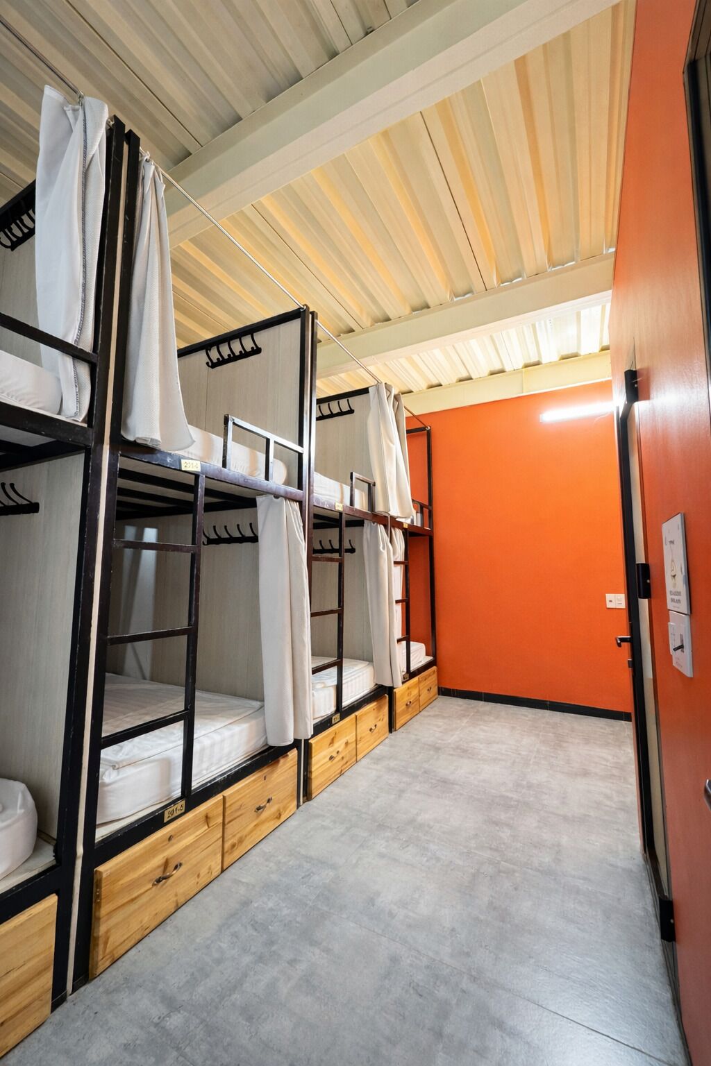 Quarto em dormitório com beliches, gavetas de madeira e uma parede laranja.