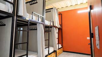 Quarto em dormitório com beliches, gavetas de madeira e uma parede laranja.
