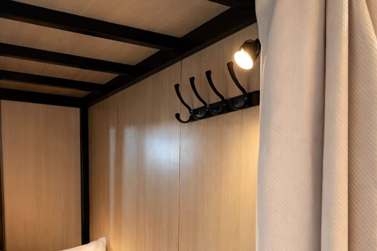 A single bed with a wooden headboard, a hanging light fixture, and a curtain partially drawn.