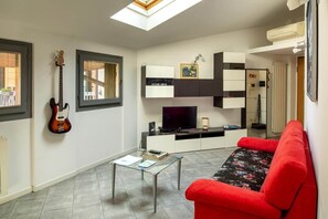 Una sala de estar moderna con un sofá rojo, una mesa de centro de vidrio, una guitarra colgada y un televisor de pantalla plana.
