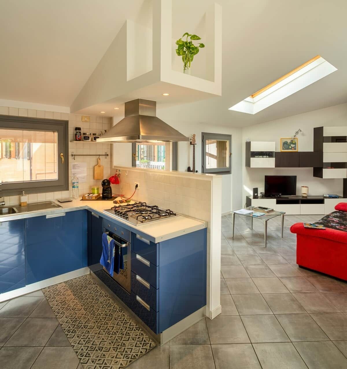 A modern kitchen with a gas stove, blue cabinets, and a large window.