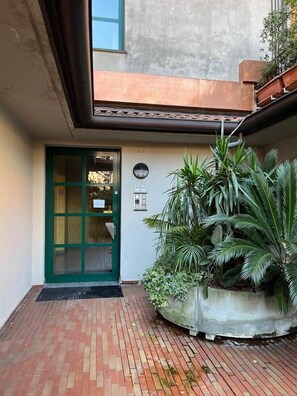 Un cortile con una porta verde, un segnale a bilancia e un fioriere con piante tropicali.