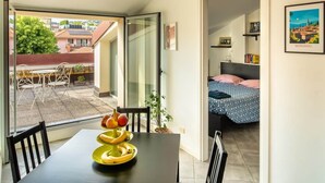 Habitació amb llit, taula de menjador amb fruita, una cadira i vista a l'exterior.
