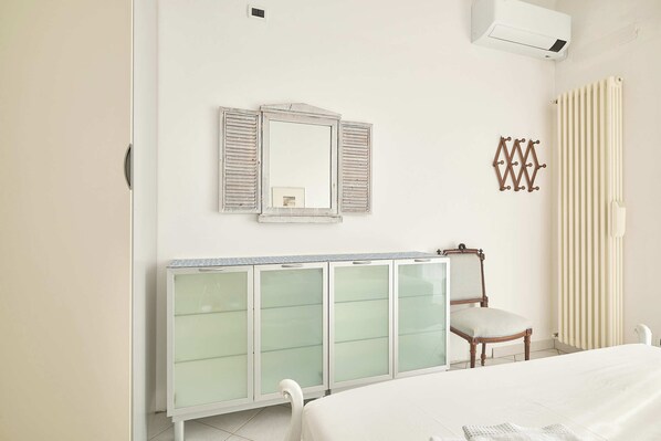 A bedroom with a bed, a bedside table, a chair, a wardrobe, a mirror, and a radiator. - Sottovento (Imperia)