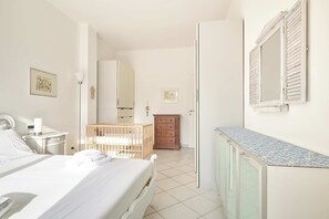 Une chambre à coucher comprenant un lit, une table de chevet, une lampe, un berceau, une commode et un miroir.